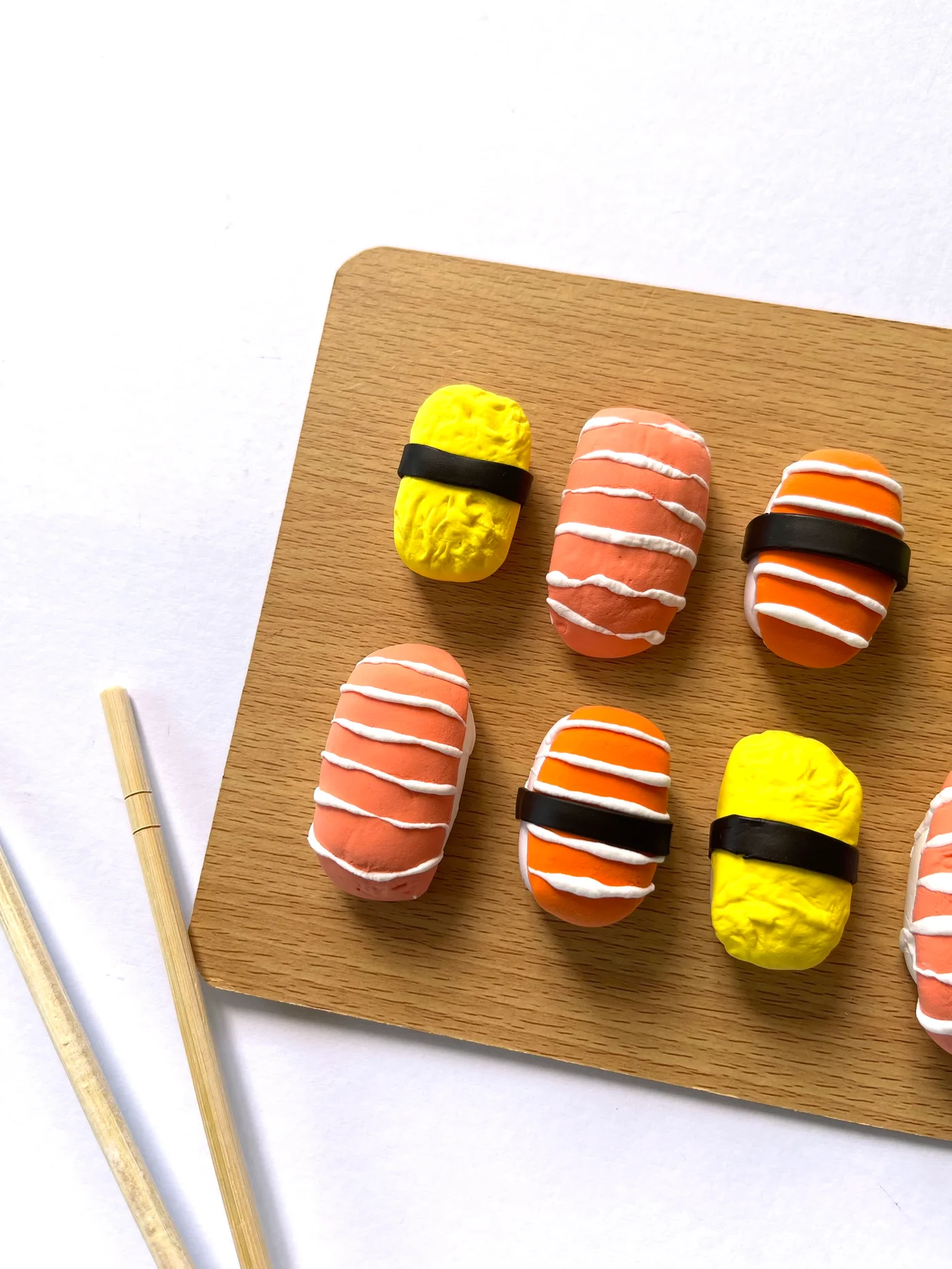 A board of air-dry clay sushi, salmon, tamago, and tuna nigiri, with chopsticks beside it