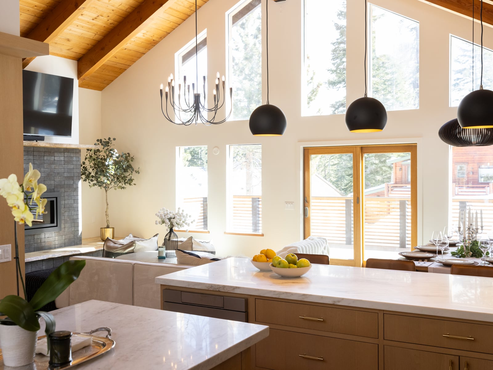 After: renovated kitchen looking out to the tall window wall, marble counter, black globe pendants and the tree view