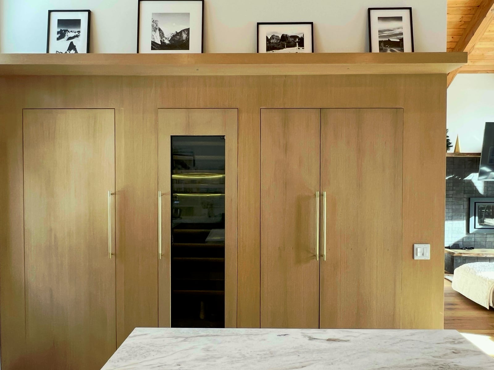 The hidden appliance wall, white oak cupboards concealing refrigeration and pantry, wine fridge visible, framed black and white photography on the ledge above