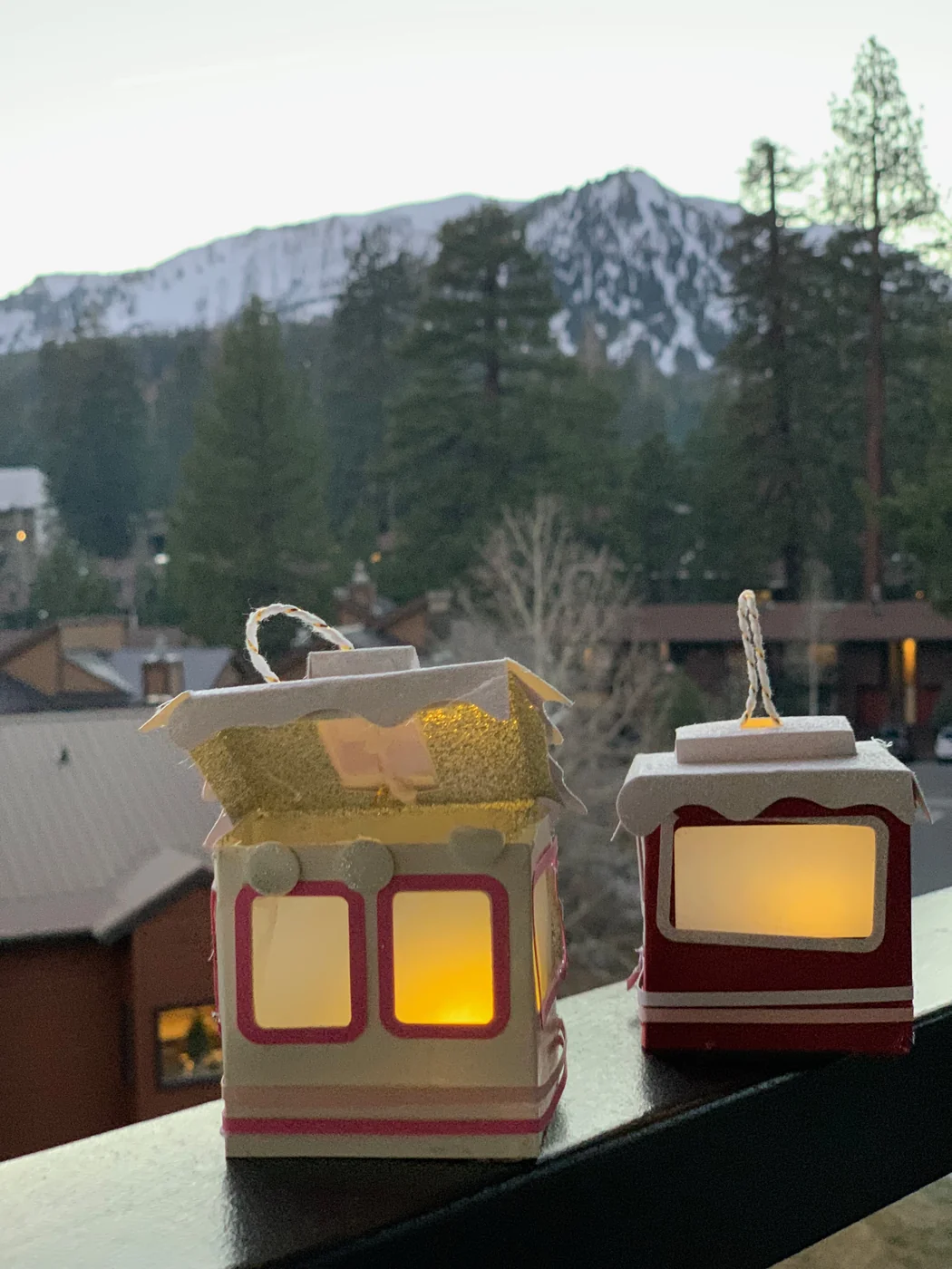 Two paper gondolas on a balcony rail, one with its roof open showing the flameless candle inside