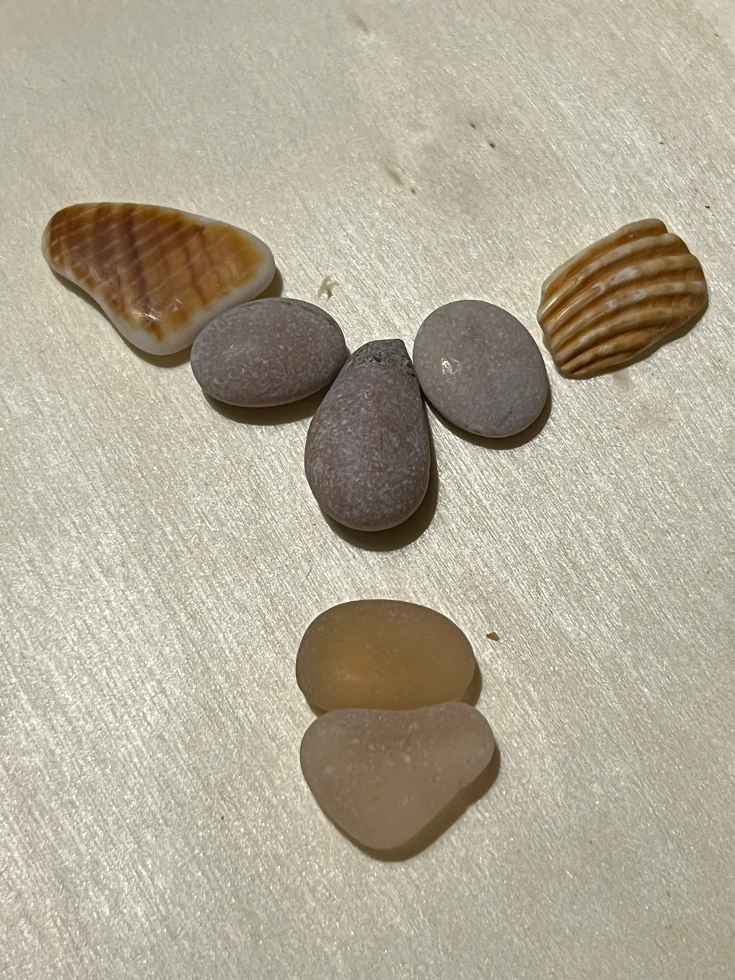 A face made of pebbles with two striped shells for eyebrows and sea glass for a mouth