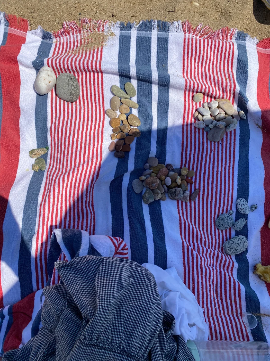 Pebbles sorted into piles by color and size on a striped beach towel