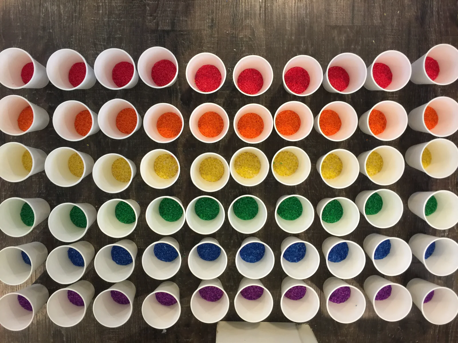 Sixty paper cups laid out in rainbow rows, each holding a scoop of colored rice for a preschool class