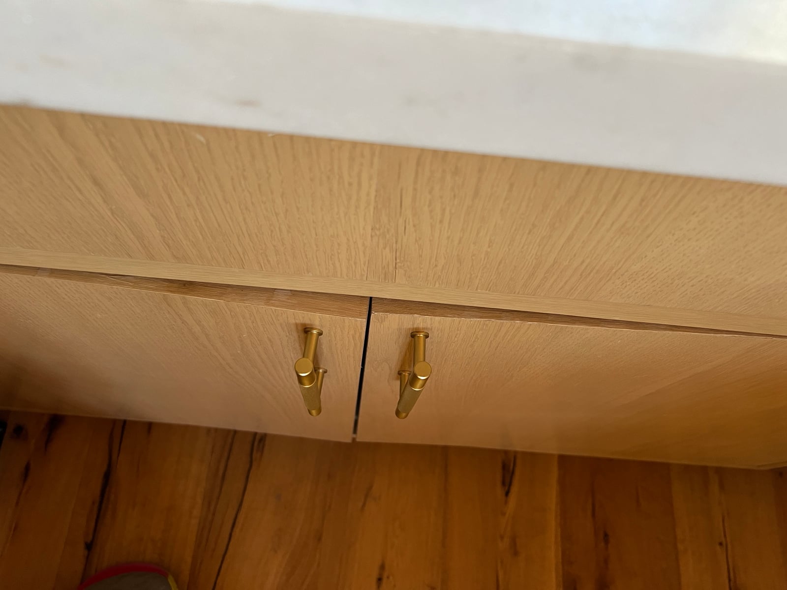 Close view of white oak cabinet fronts with brass pulls, showing the uneven reveal where the door has warped