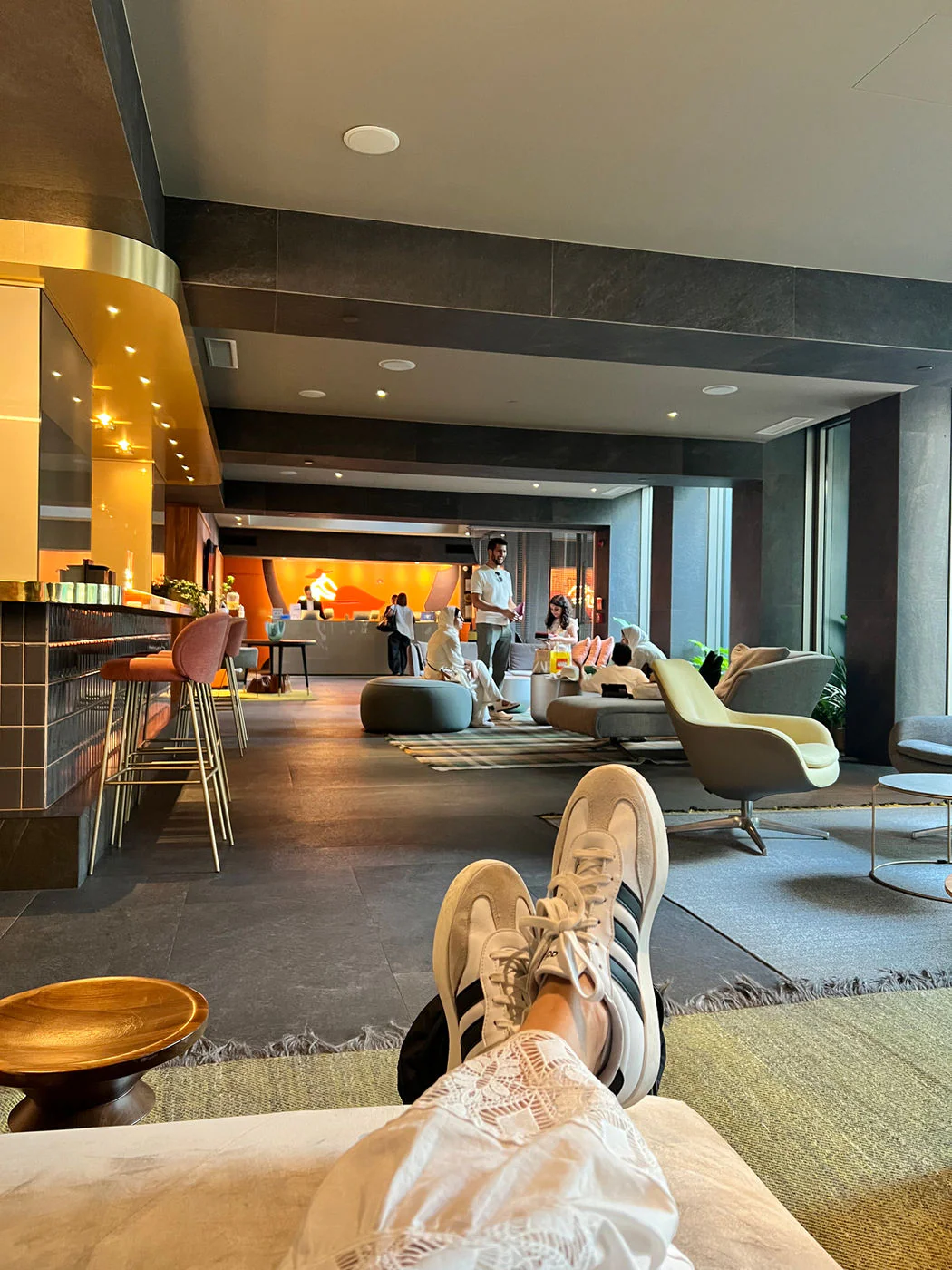 A relaxed view across a modern hotel lobby with lounge chairs and a bar, taken with feet propped up.