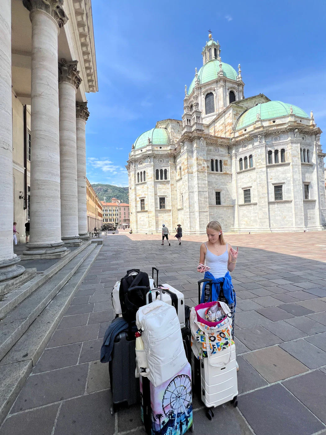 A pile of suitcases and bags stacked in a stone piazza in front of Como Cathedral.