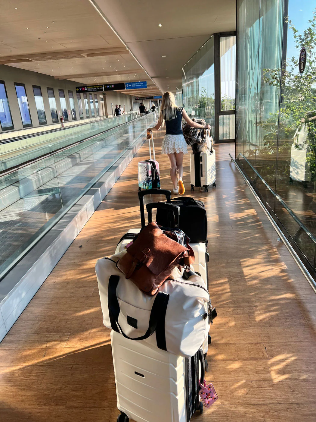 A row of six wheeled suitcases and bags lined up on a sunlit airport moving walkway.